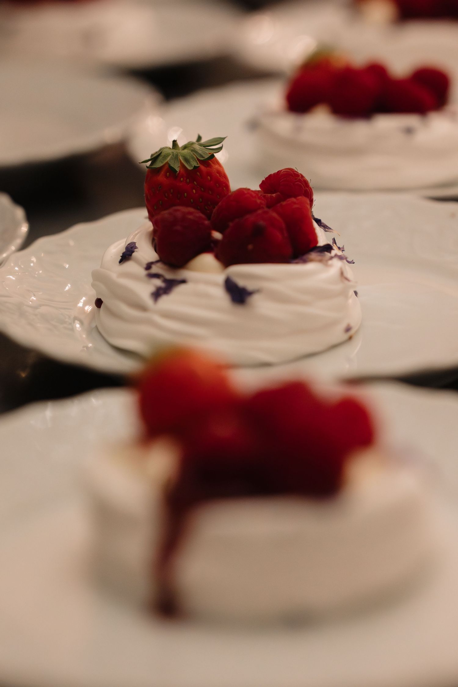 Close-up of elegant pavlova dessert topped with fresh strawberries and raspberries on white plate.