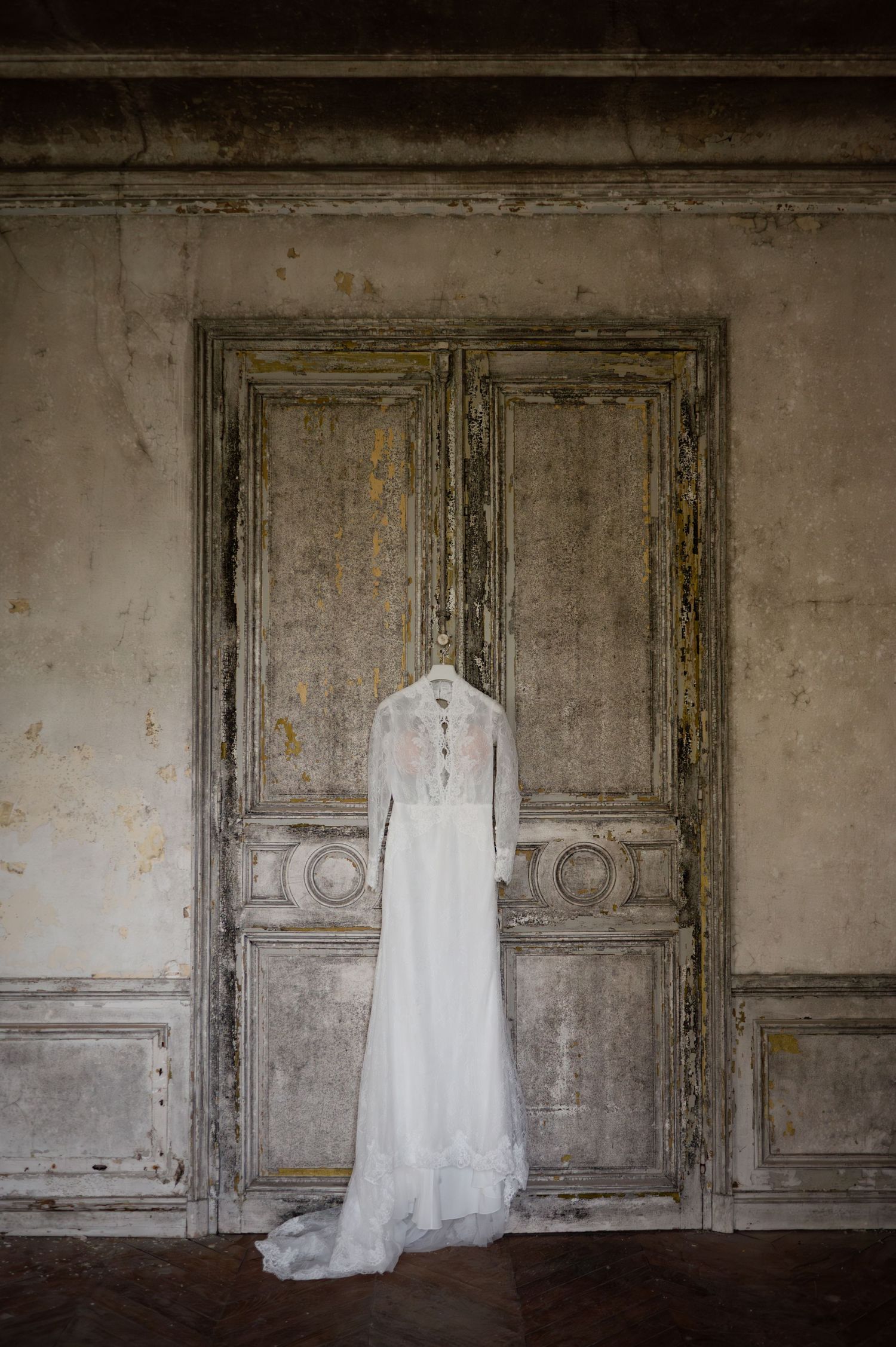 Elegant long-sleeve white wedding dress hanging on rustic antique distressed wooden door.