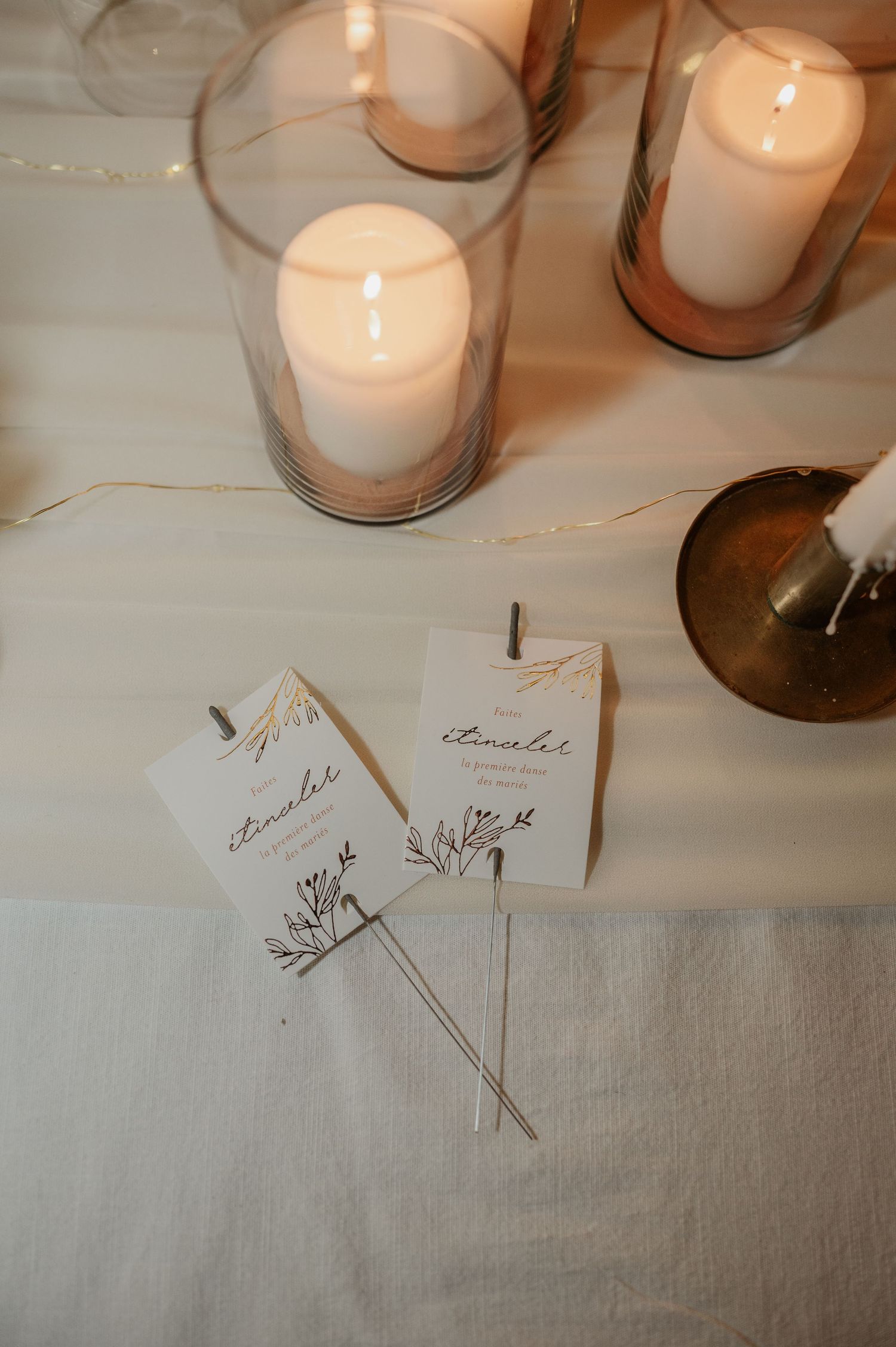 Wedding itinerary cards with botanical design displayed beside glowing candles on white linen.