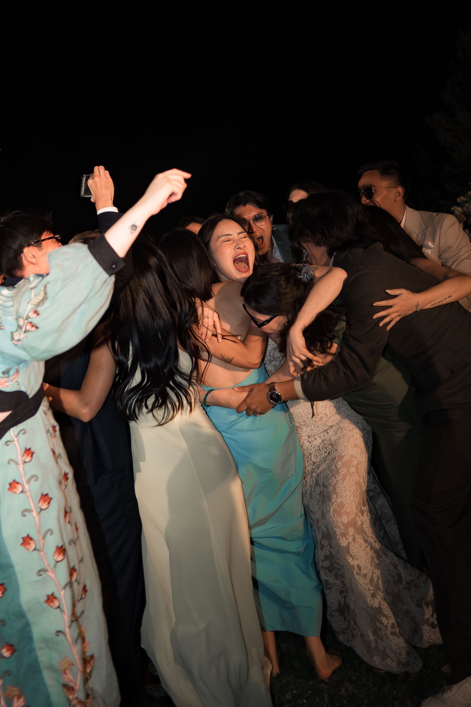 Guests dancing and celebrating joyfully at an outdoor wedding reception at night.