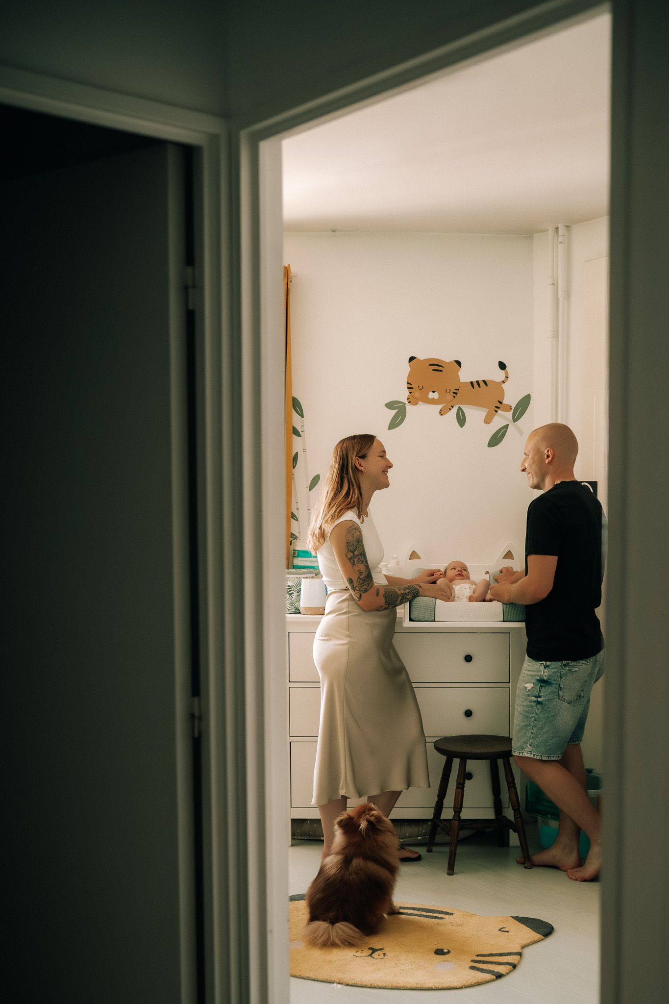 New parents smiling at each other over their newborn on a changing table in a nursery.