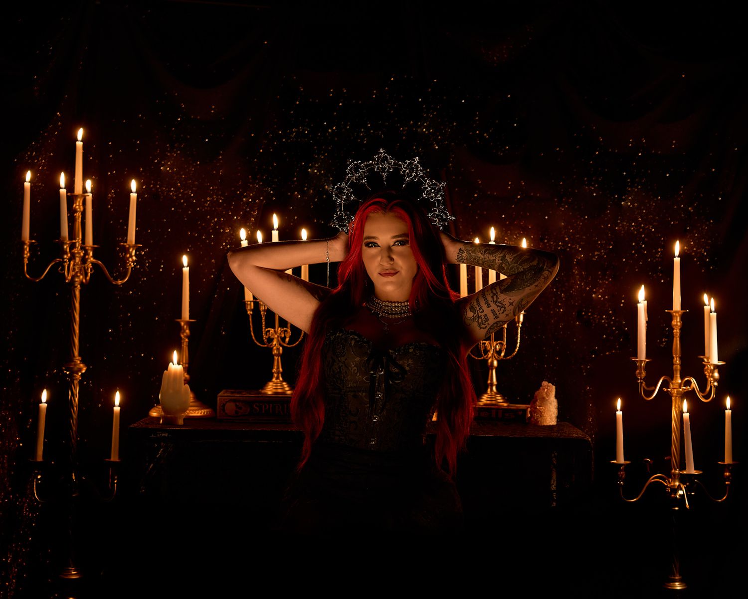 Woman with red hair in a black corset surrounded by candles and candelabras in a gothic setting.