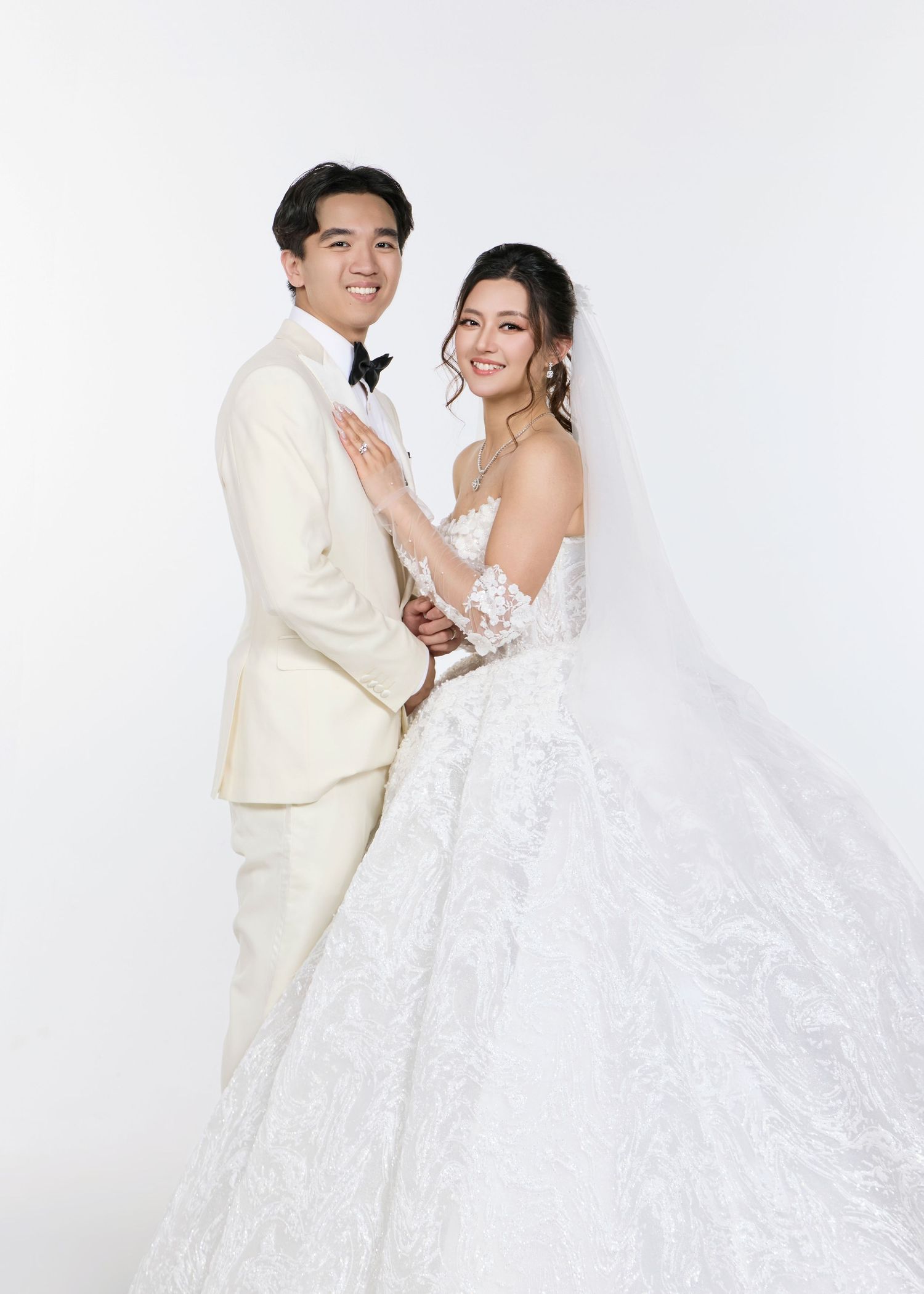 Smiling couple in wedding attire, groom in ivory tuxedo and bride in lace ball gown.