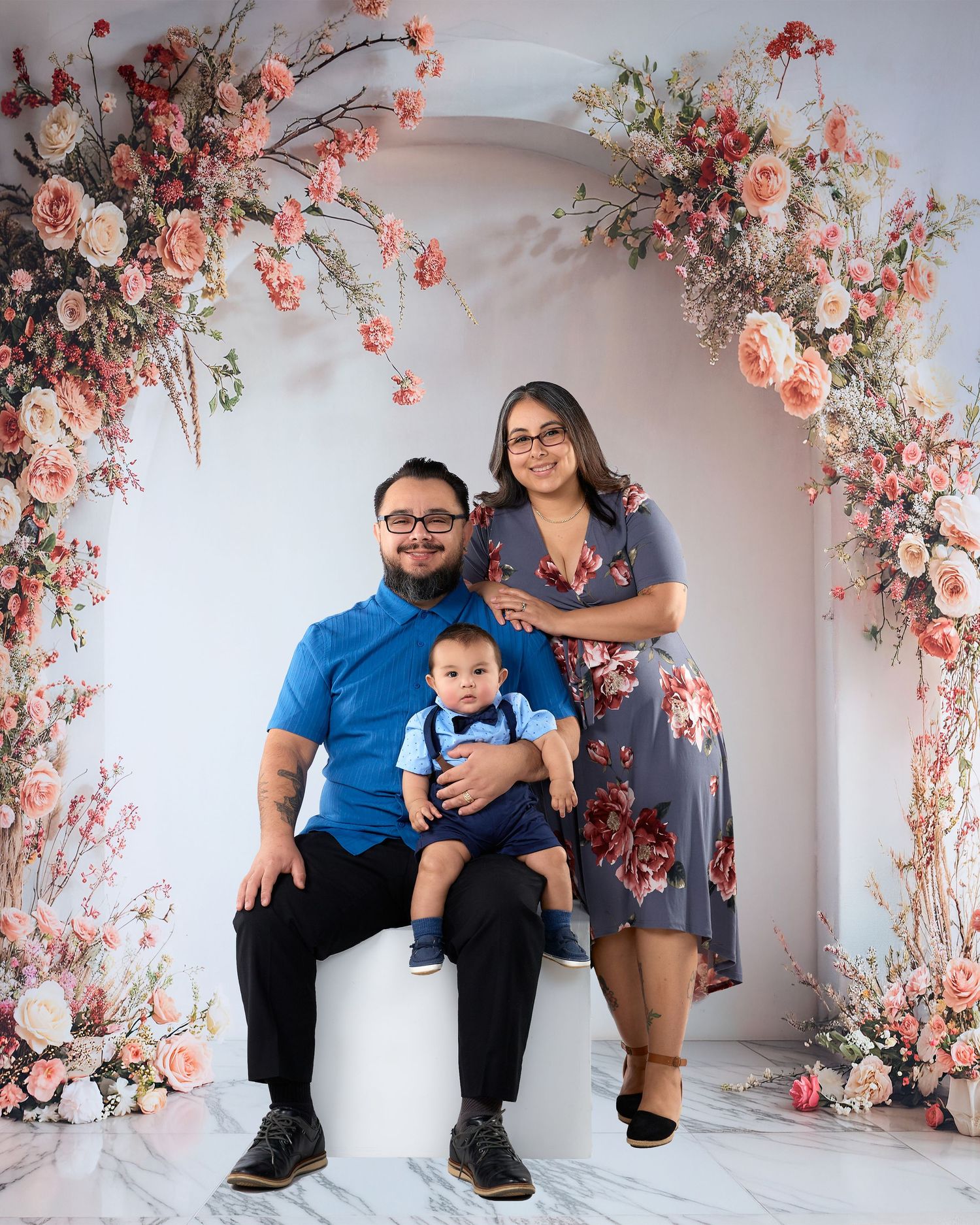 Family portrait with parents and baby under a floral arch with pink roses.