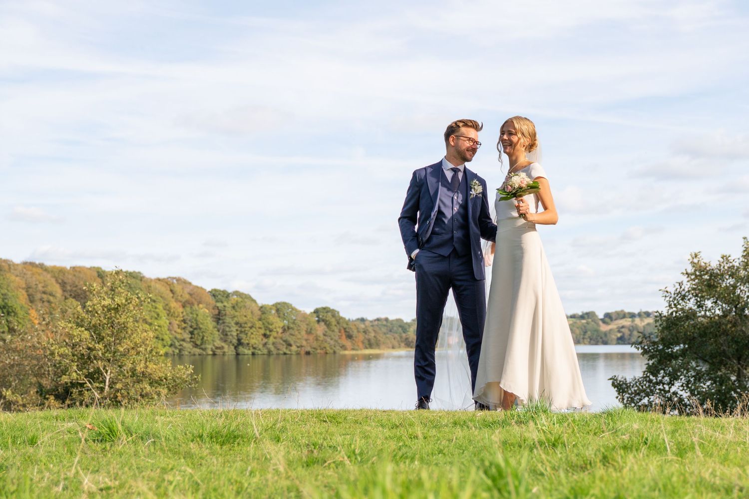 Brudepar fotograferet sammen ved søen på deres bryllupsdag