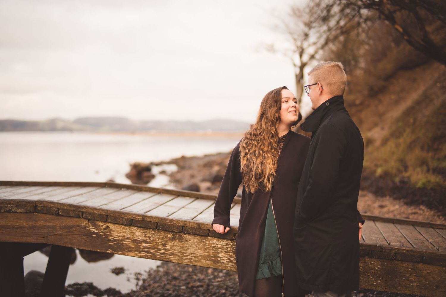 Par står tæt sammen ved vandet under deres prøvefotografering inden brylluppet