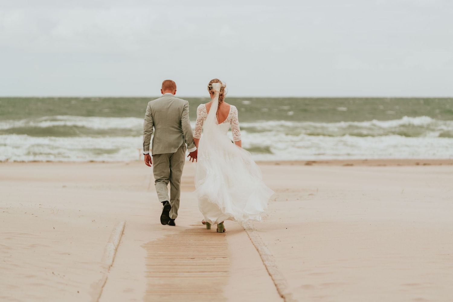 Newlyweds walking hand in hand along a windswept Danish beach after their wedding