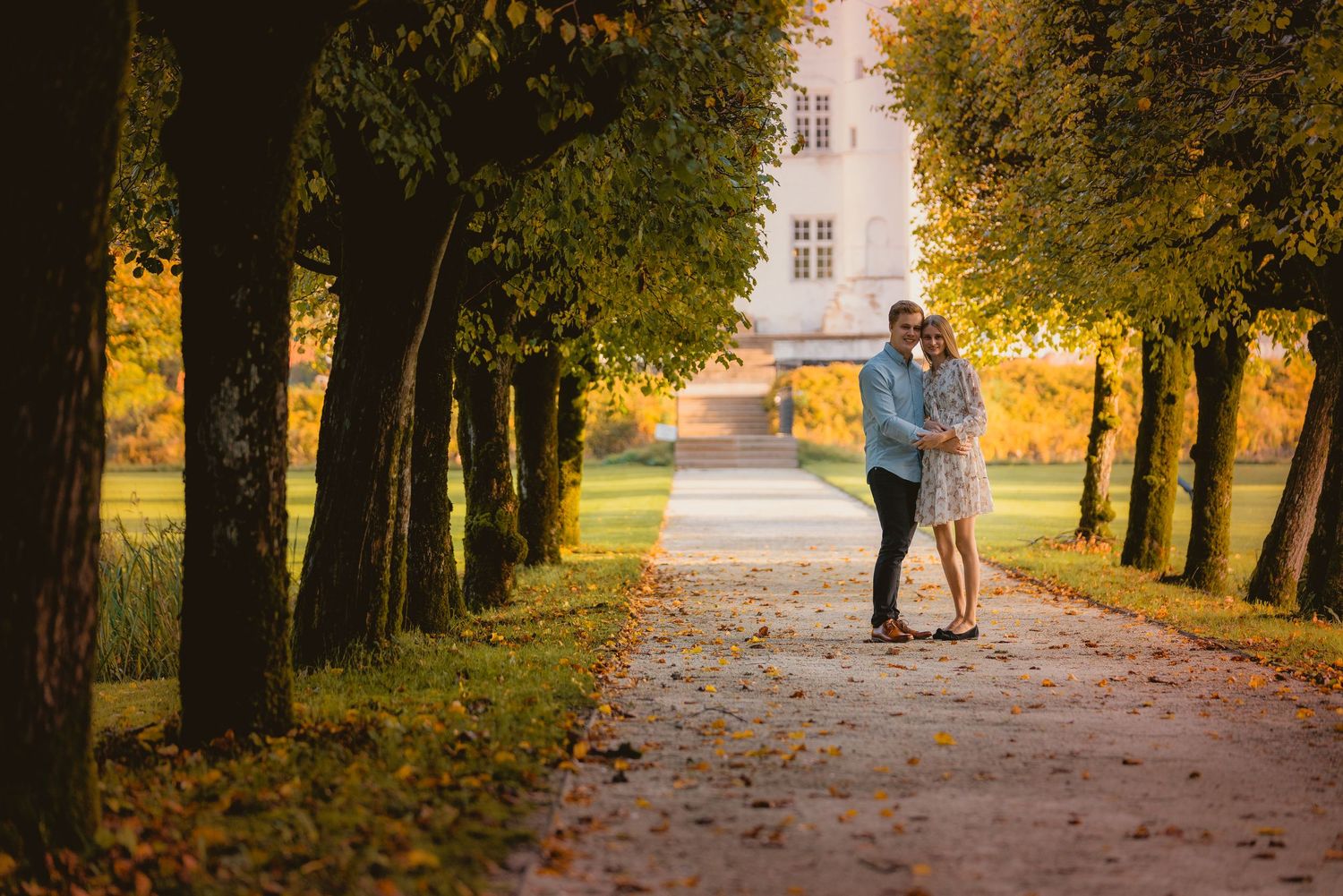 Ungt par fotograferet i varmt efterårslys ved en allé
