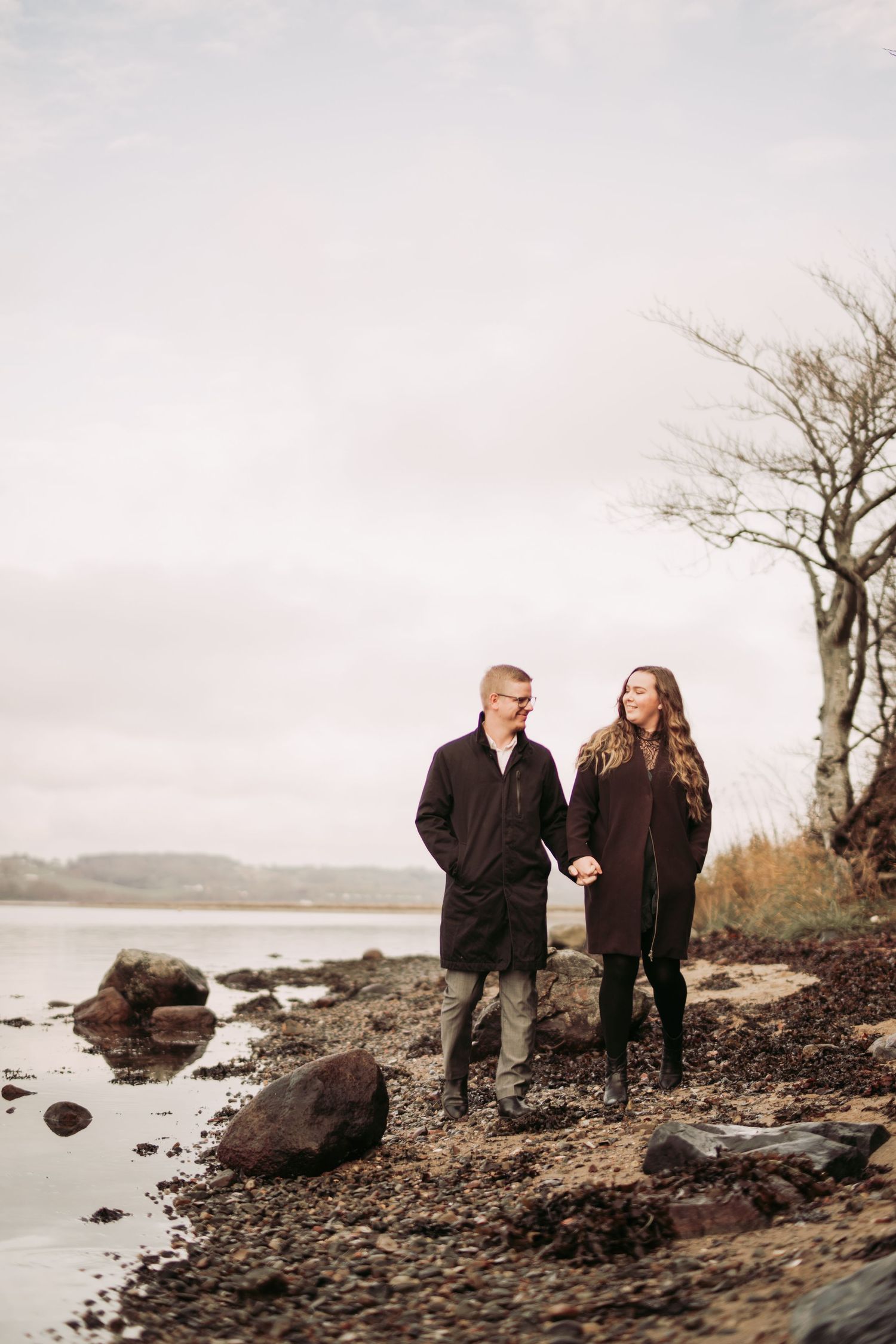 Par går hånd i hånd langs vandet under en fotografering inden brylluppet