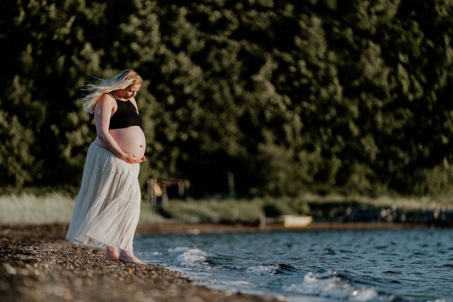 Gravid kvinde stående ved vandkanten i det varme aftenslys
