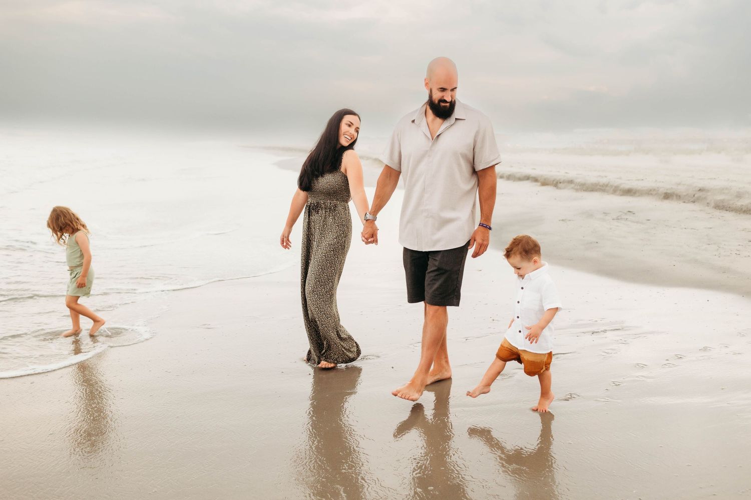 A family walks together along a misty beach shoreline while waves gently lap at their feet.