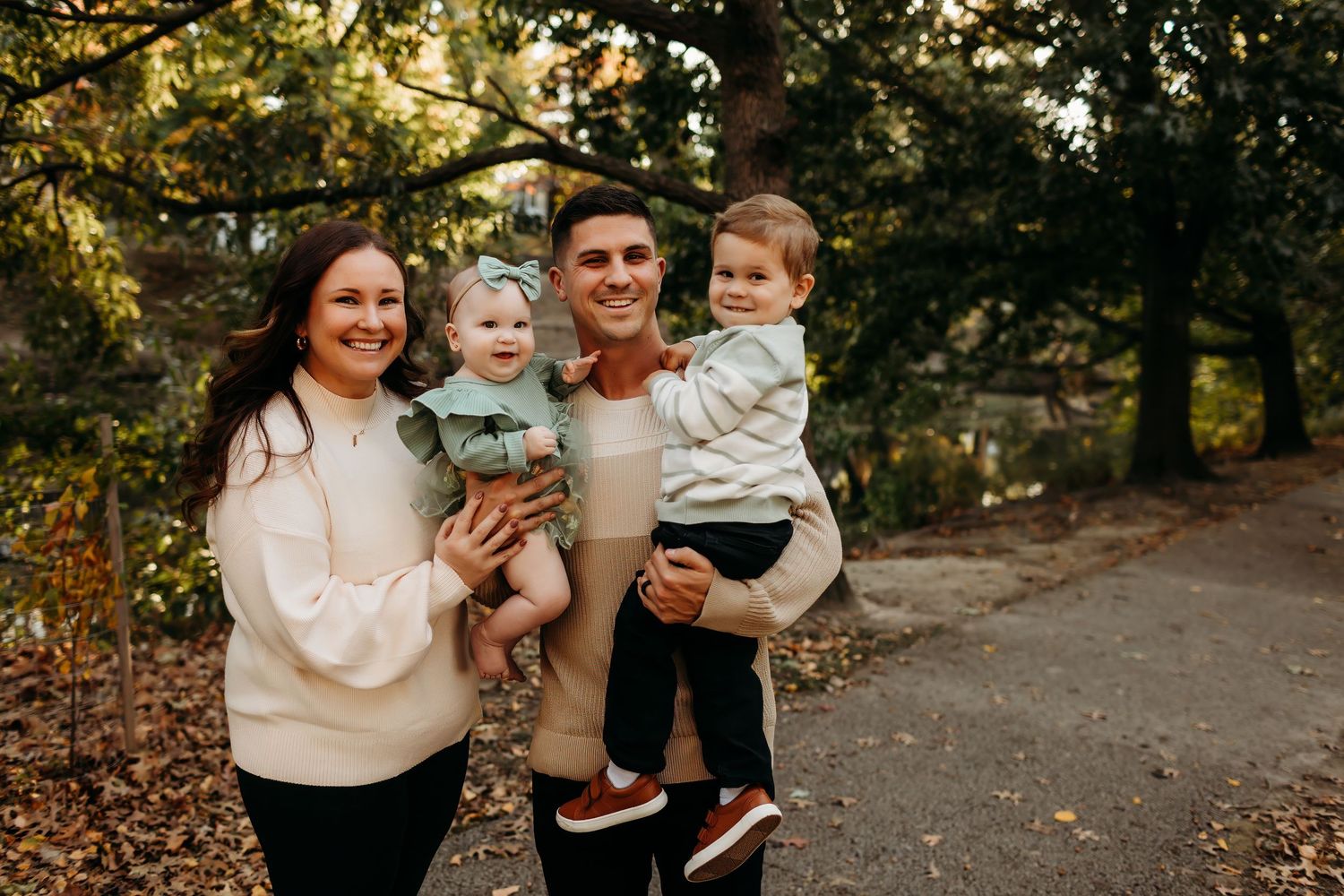 A smiling family of four poses outdoors in autumn, parents each holding a young child in Delaware County, pa
