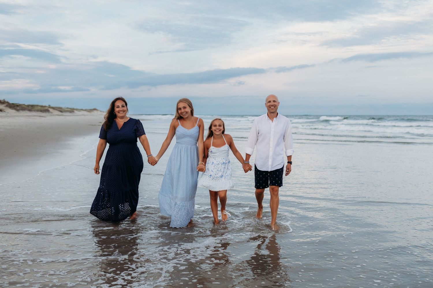 Happy family of four holding hands and walking together along a scenic ocean beach at dusk.