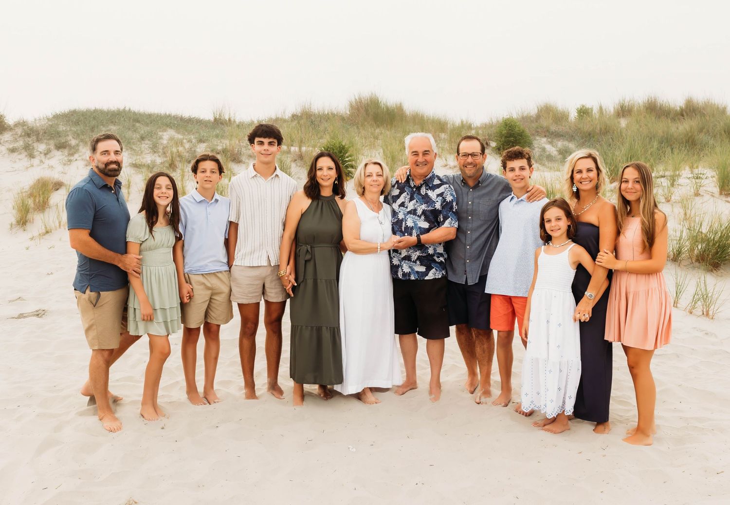 A group of people standing together on a sandy beach at sunset wearing casual summer attire.