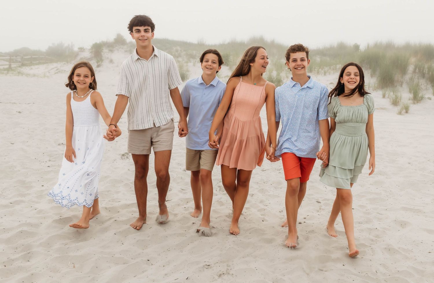 A group of friends walking barefoot together along a misty coastal beach during sunset.