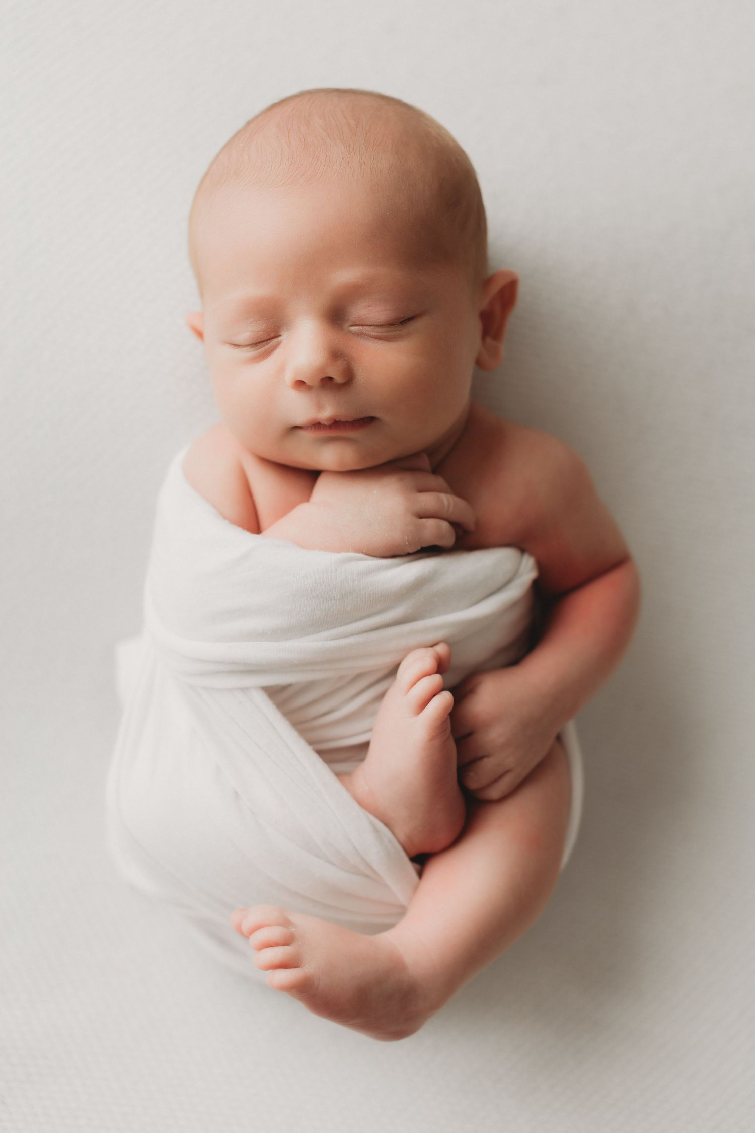 Peaceful newborn baby swaddled in white wrap sleeping on soft white background.