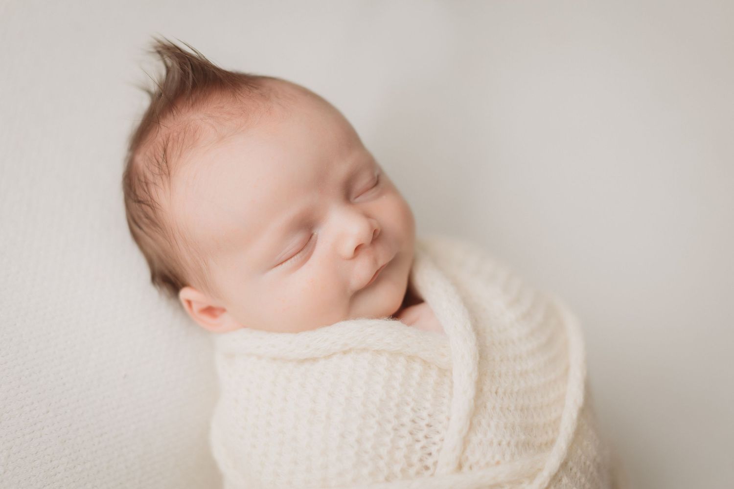 Serene sleeping newborn baby boy swaddled in cream knit wrap on white background.