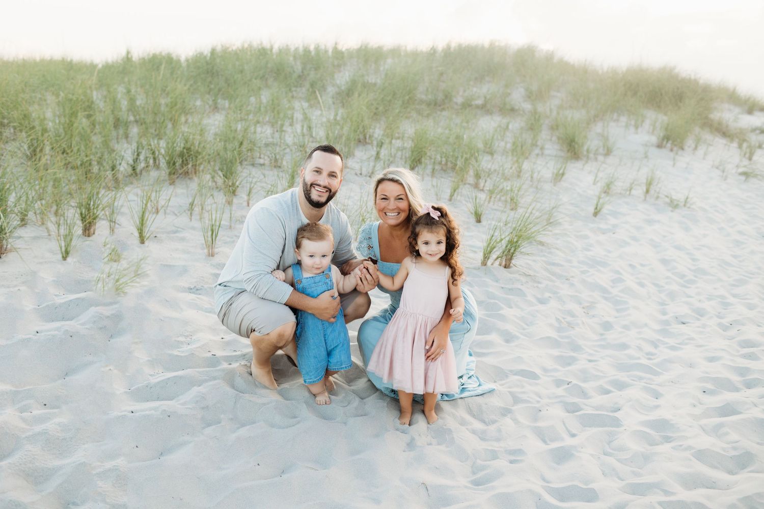 Beach family portrait with sand dunes and sea grass in the background during golden hour.