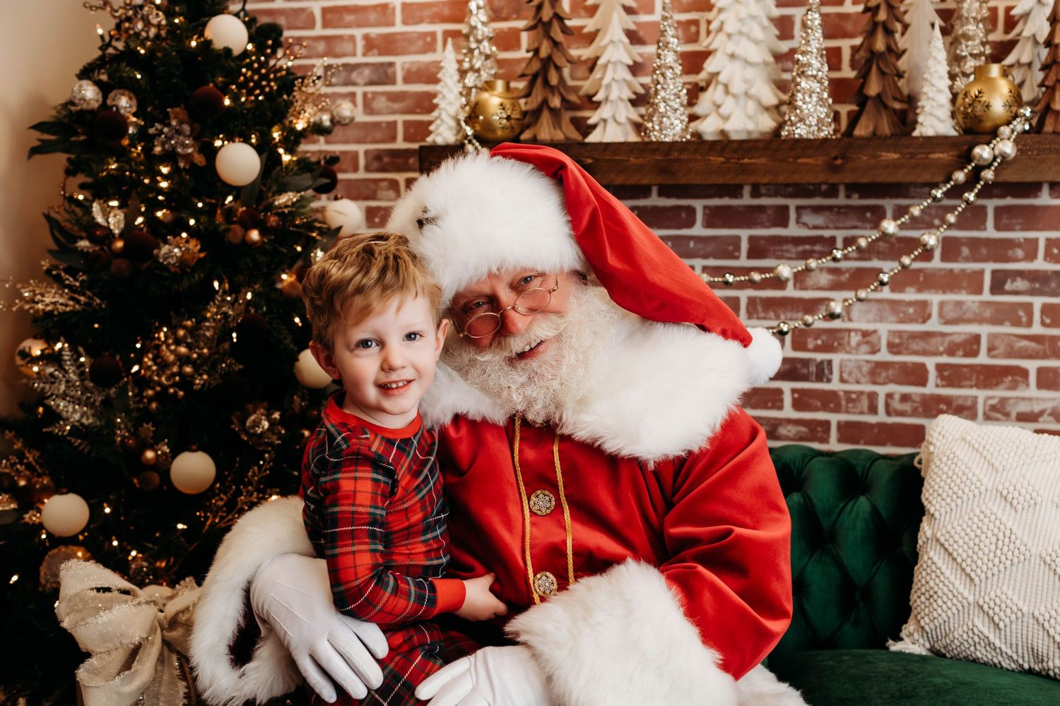 Festive holiday scene with Santa Claus in traditional red suit seated by decorated Christmas tree with ornaments and brick wall.