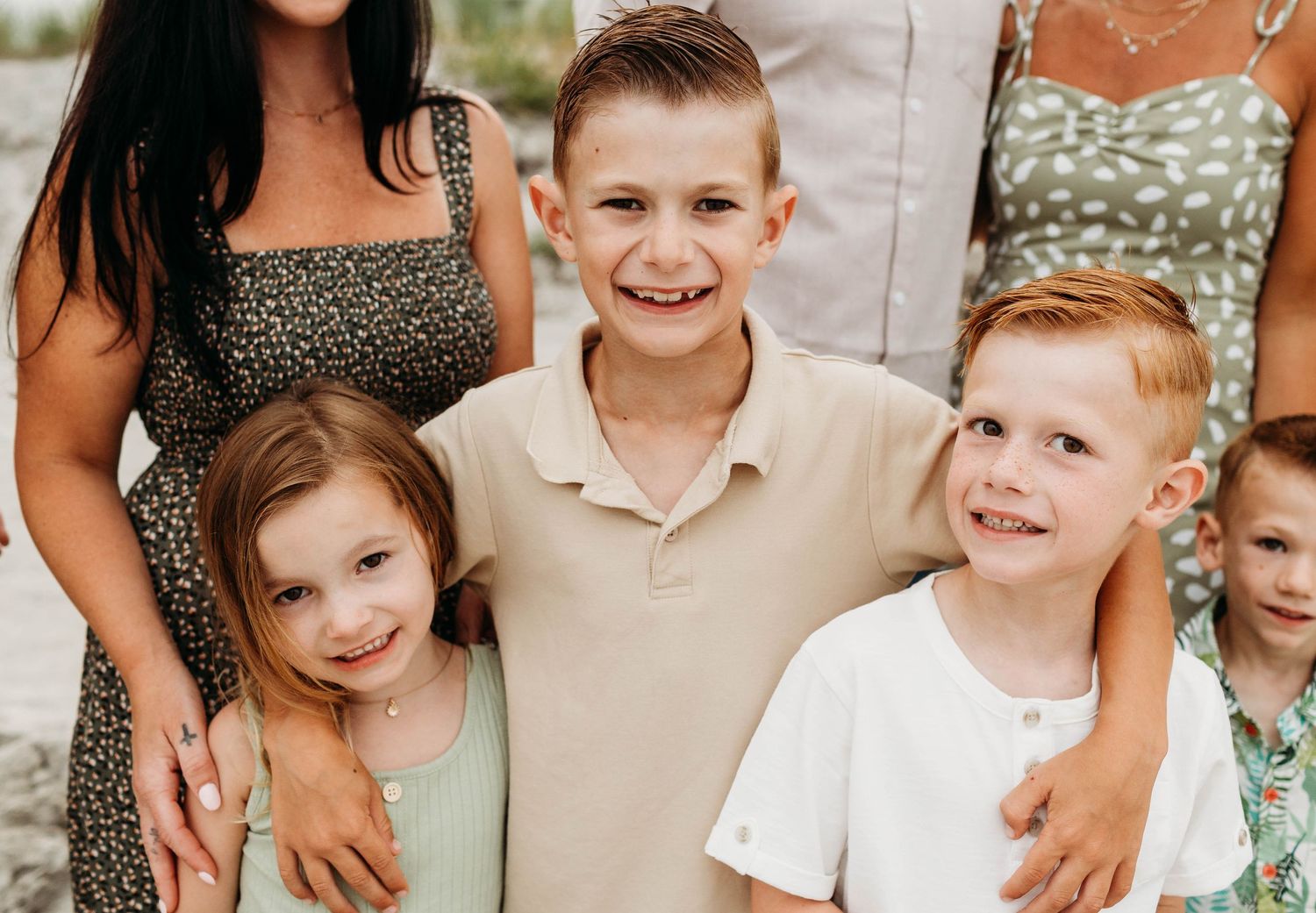 Family members smiling together outdoors wearing coordinated casual summer outfits in neutral and pastel tones.