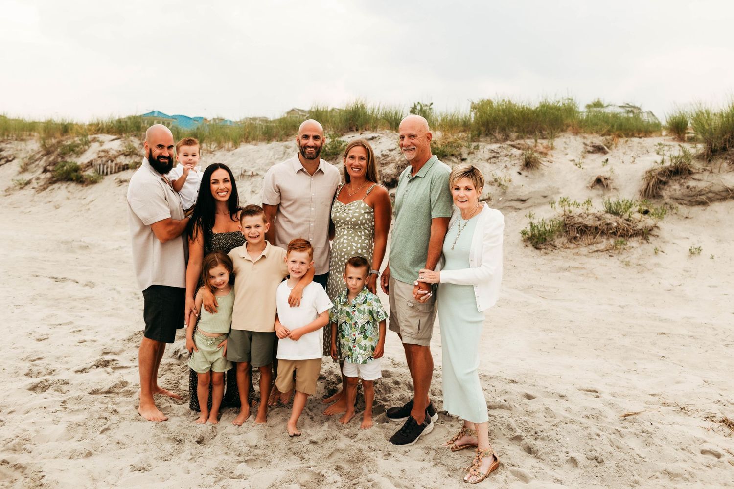 Family group standing together on a sandy beach with dunes in the background during golden hour.