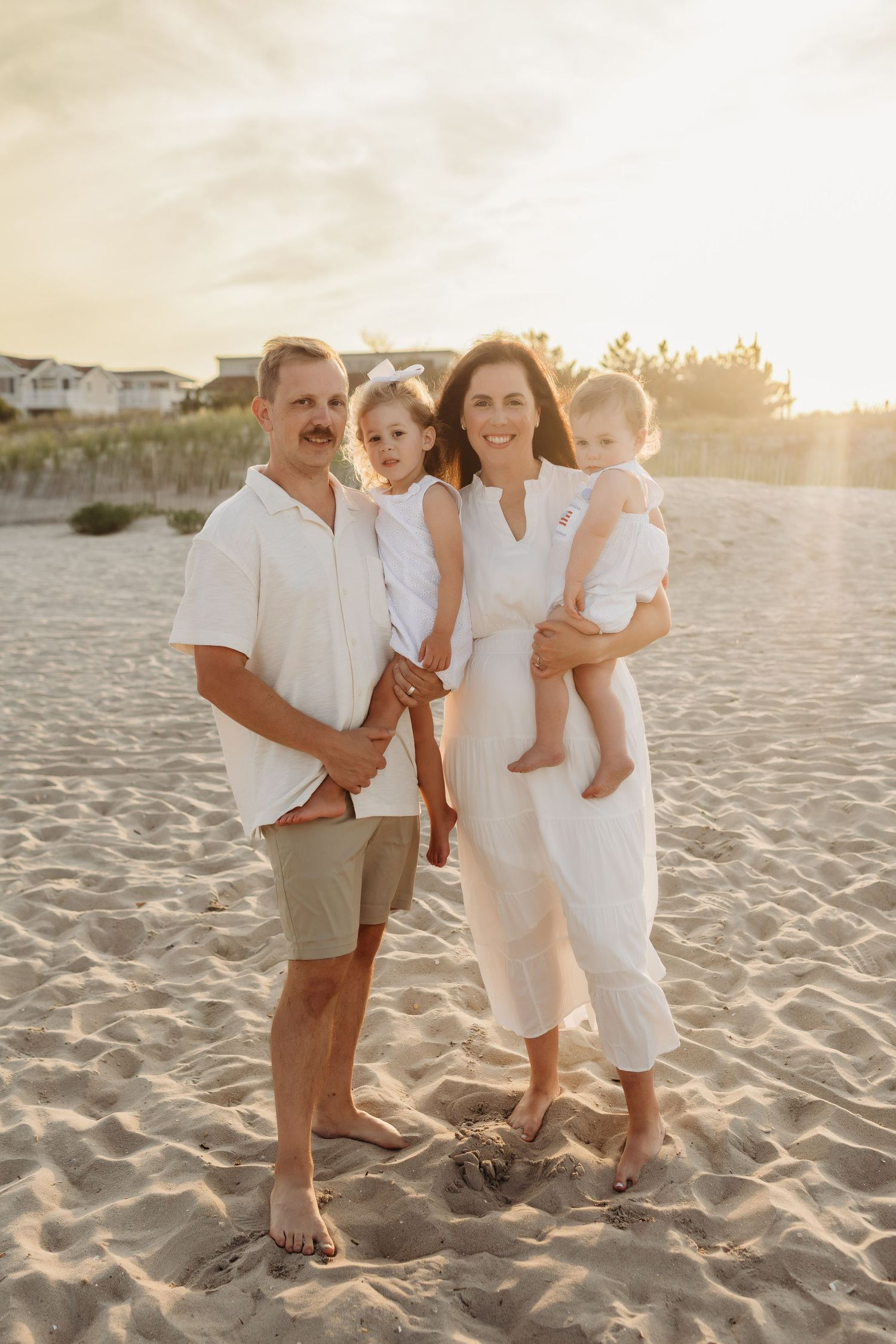 Family of four posing on sea isle city beach at golden sunset, wearing coordinated white and neutral outfits in