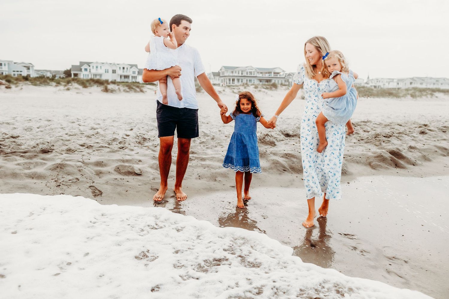 A family holds hands while walking together on a sunny beach during golden hour along the coastline.
