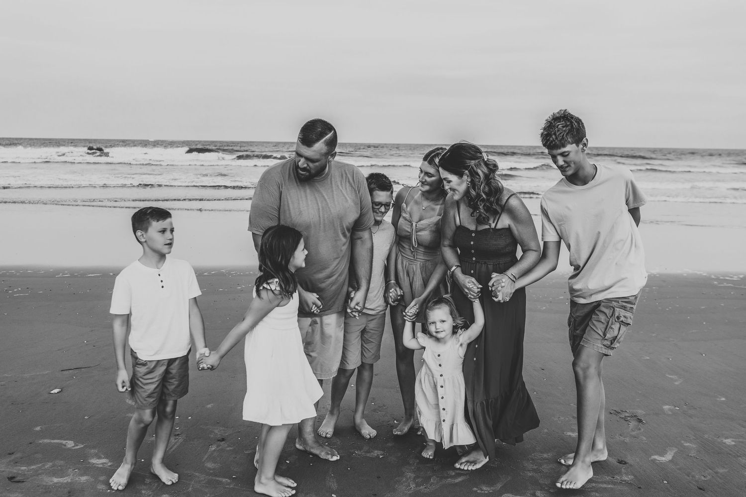 Black and white photo of a large family laughing and holding hands on a beach.