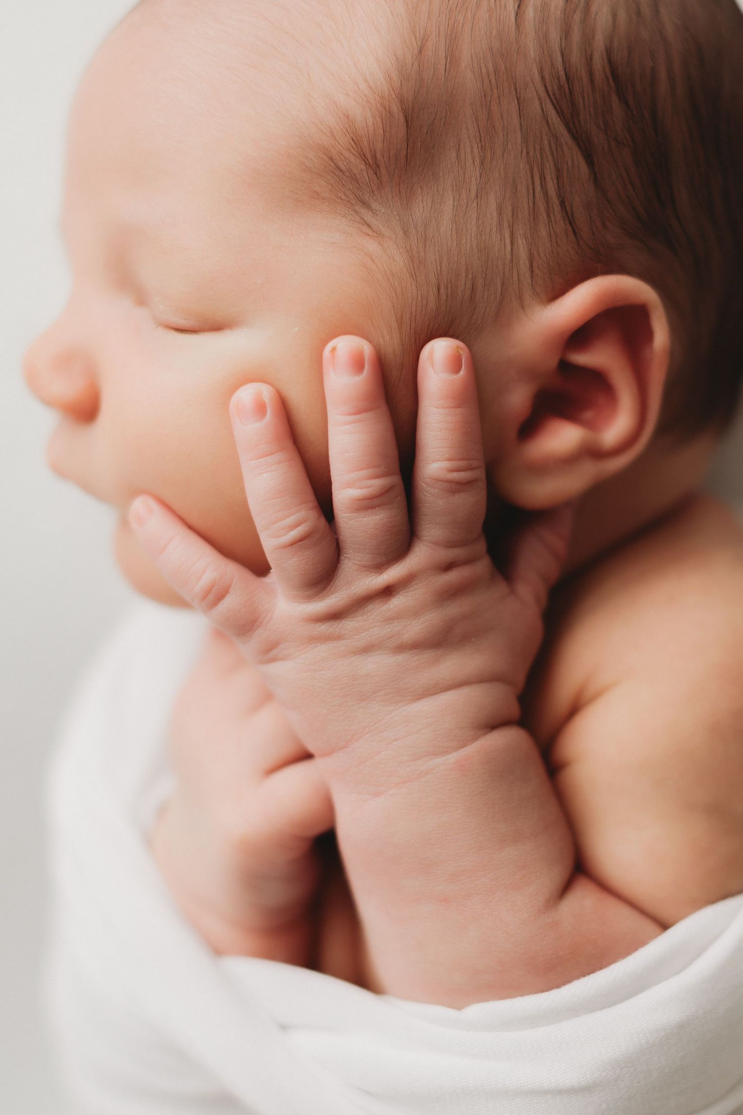 Macro close-up of peaceful sleeping newborn baby tiny hand resting against cheek.