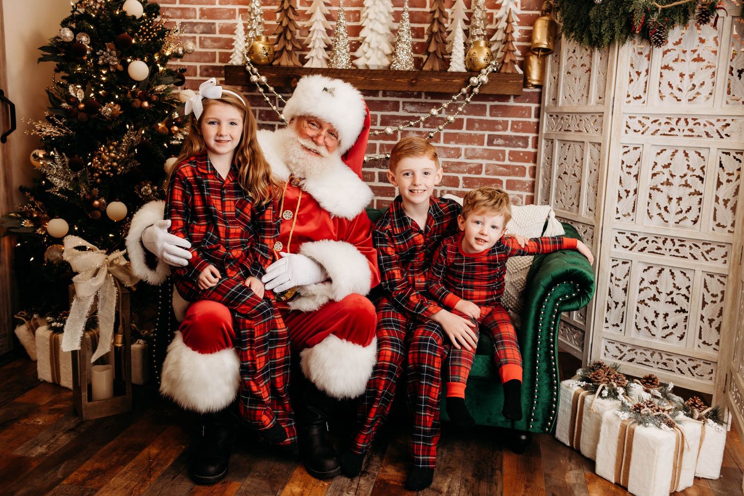 Holiday portrait with Santa Claus and children in matching buffalo plaid pajamas next to Christmas tree and decorations.