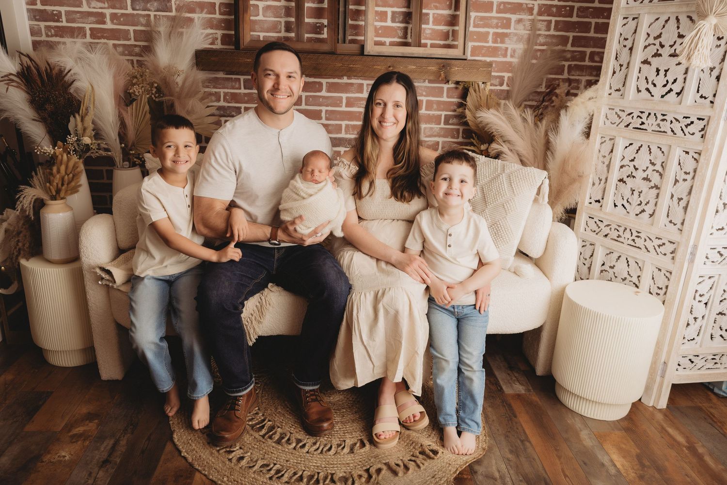 Family of five posing for a professional portrait in a cozy boho studio with brick walls and neutral decor.