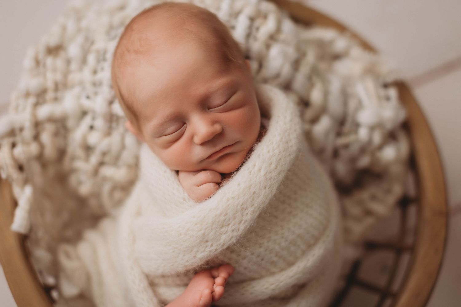 A peaceful sleeping newborn wrapped snugly in a white swaddle blanket against a neutral backdrop.