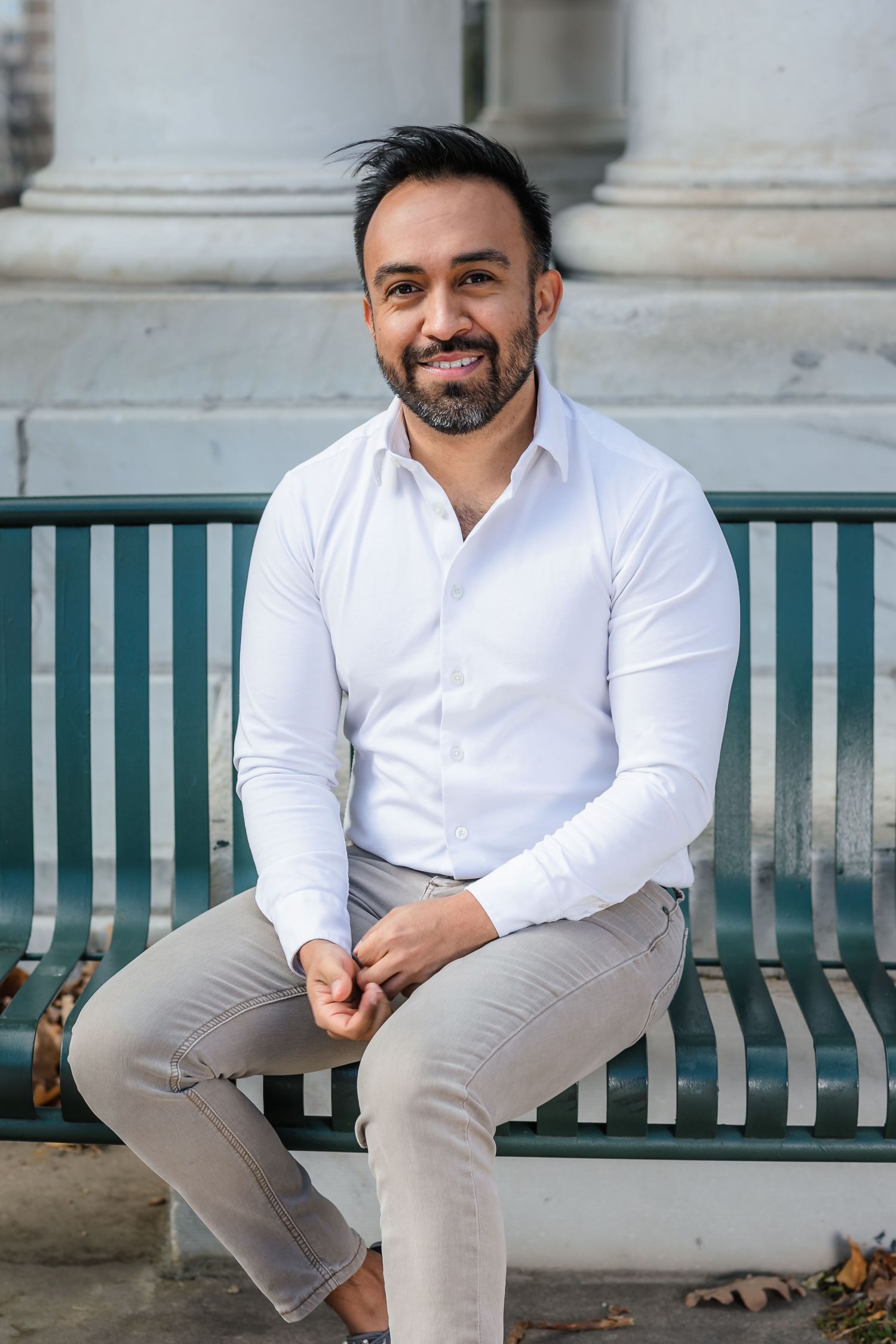 Professional executive headshot of a man sitting on a green bench outdoors in Northern Colorado
