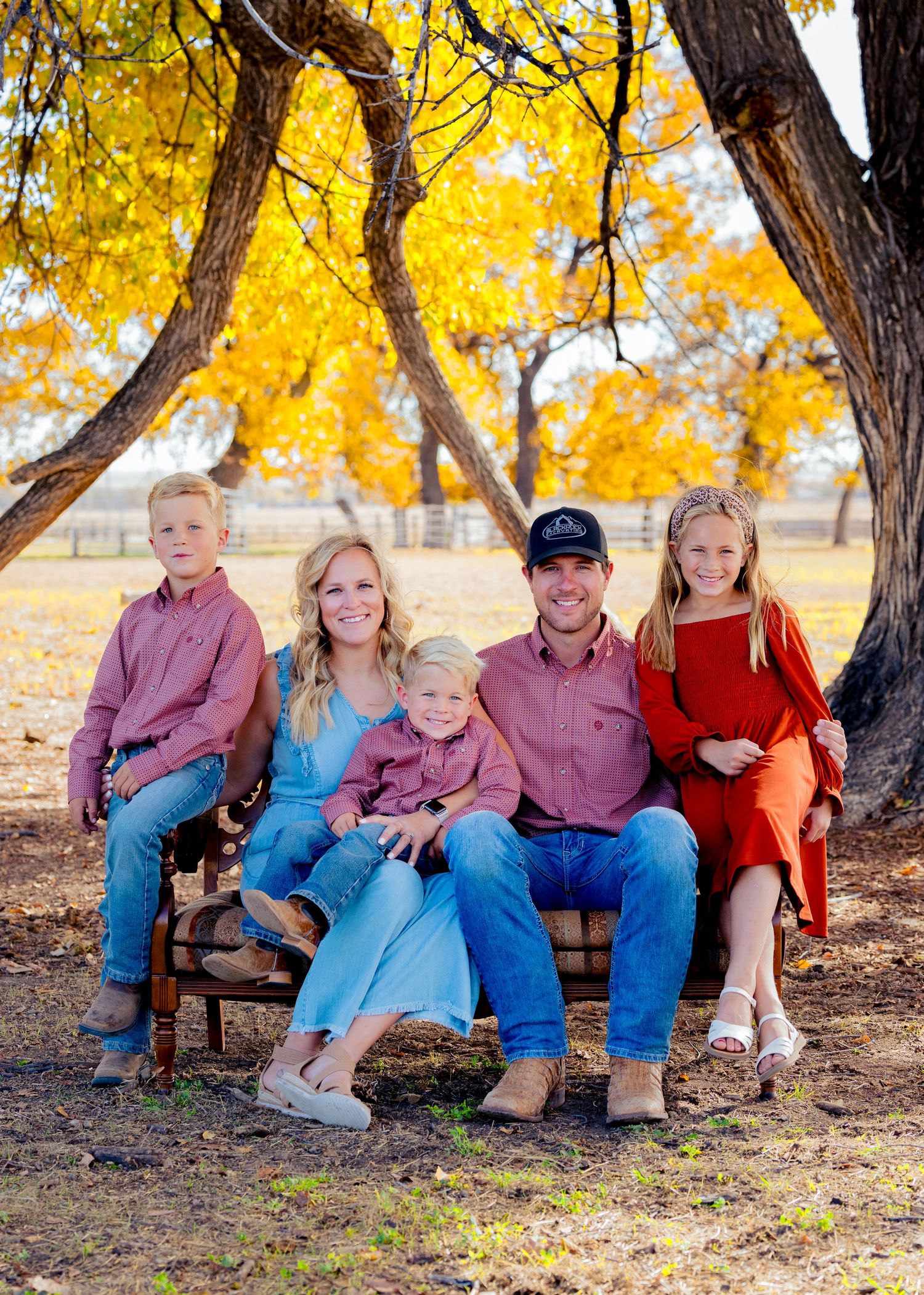 Family of five smiling together on a bench surrounded by bright autumn trees in Northern Colorado