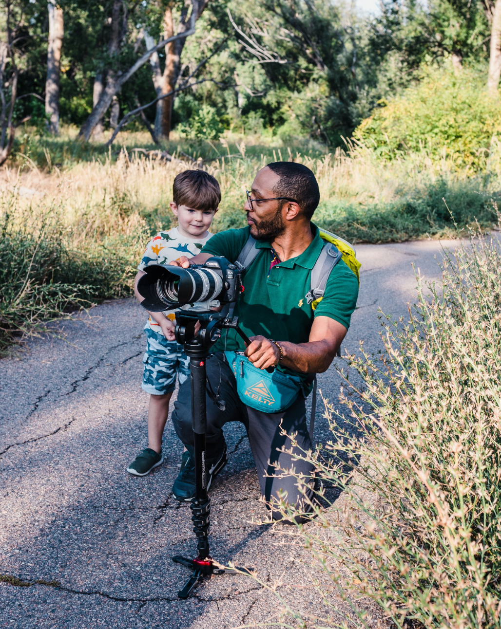 Behind the scenes of photographer showing a camera preview to a young child during an outdoor family session in Northern Colorado