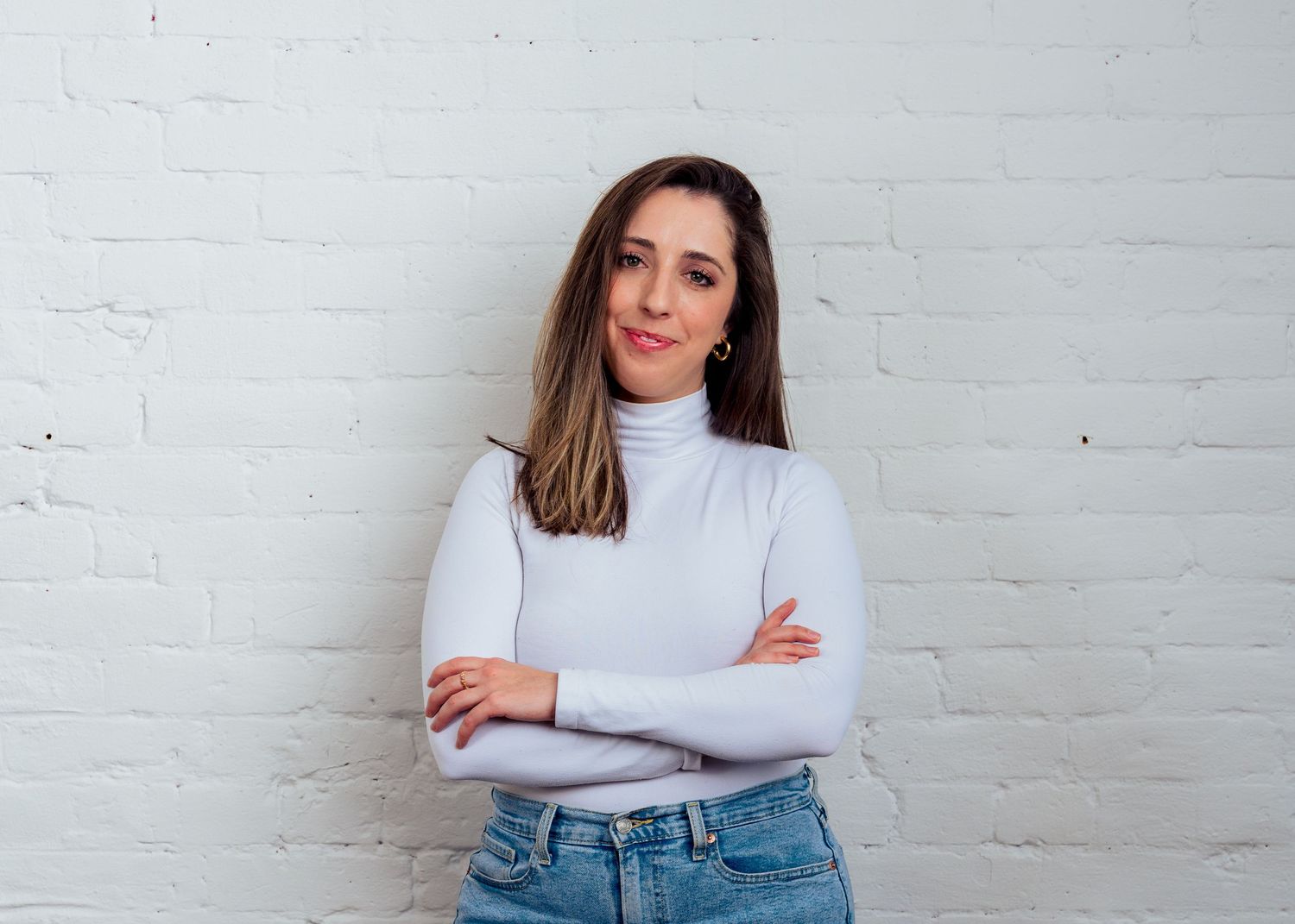 Professional executive headshot of a woman with crossed arms against a white brick wall in Northern Colorado