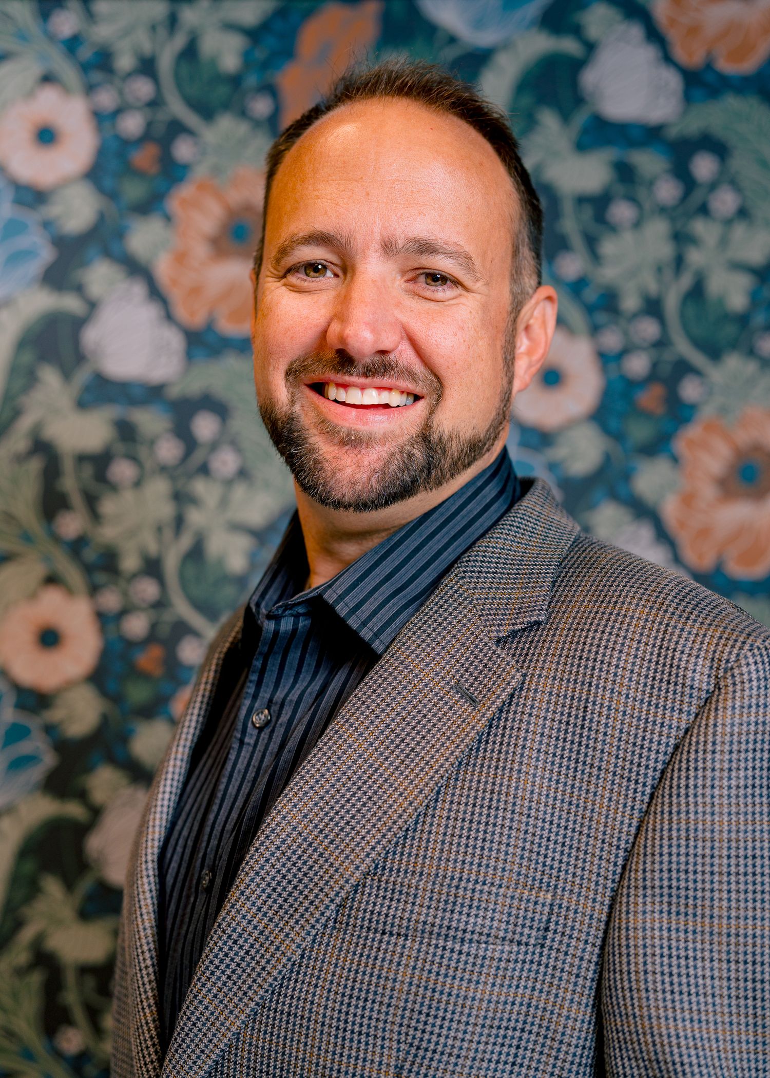 Executive headshot of a smiling man in a blazer against a patterned studio backdrop in Northern Colorado