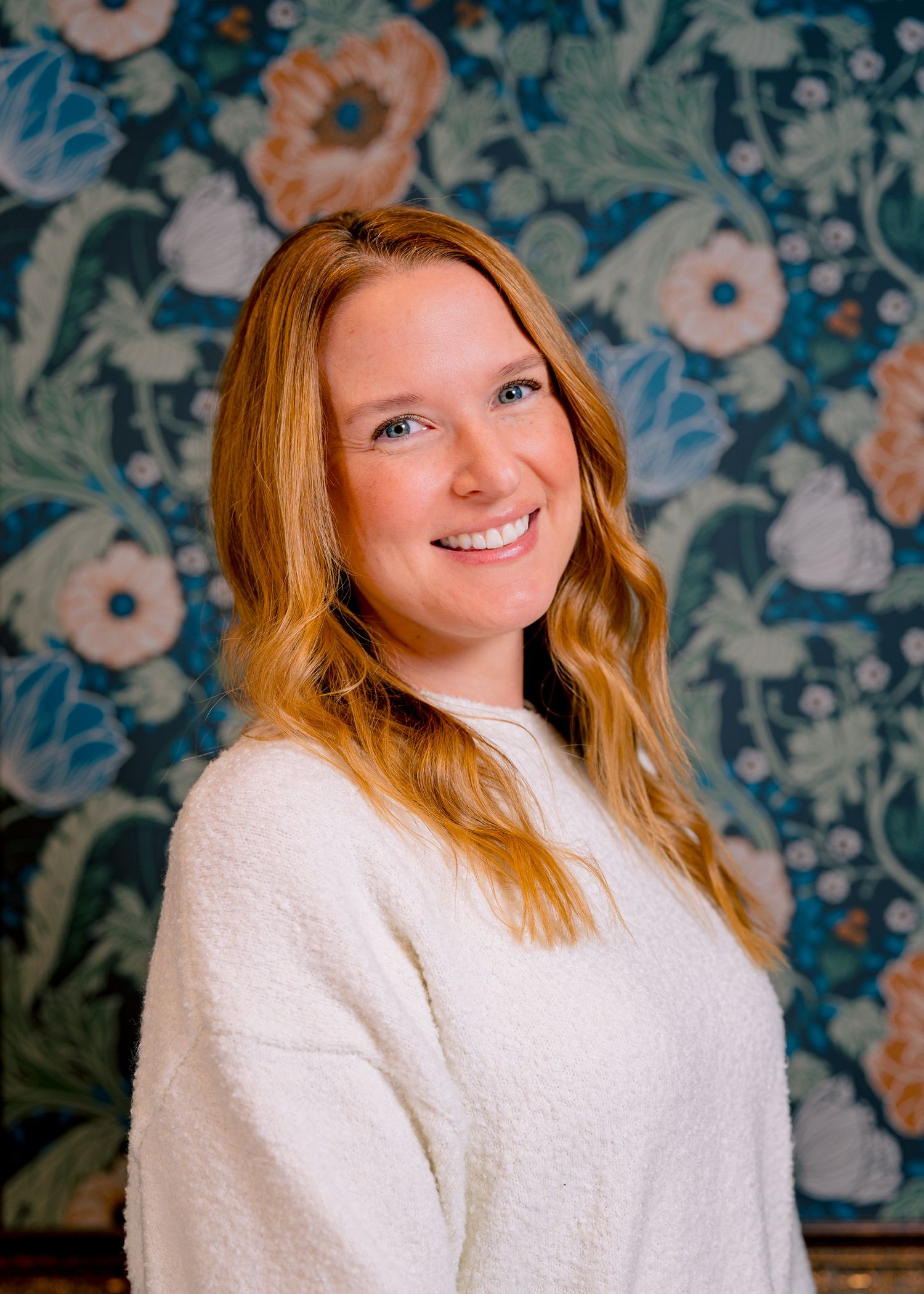 Professional corporate headshot of a smiling woman in a cream sweater against floral backdrop in Northern Colorado