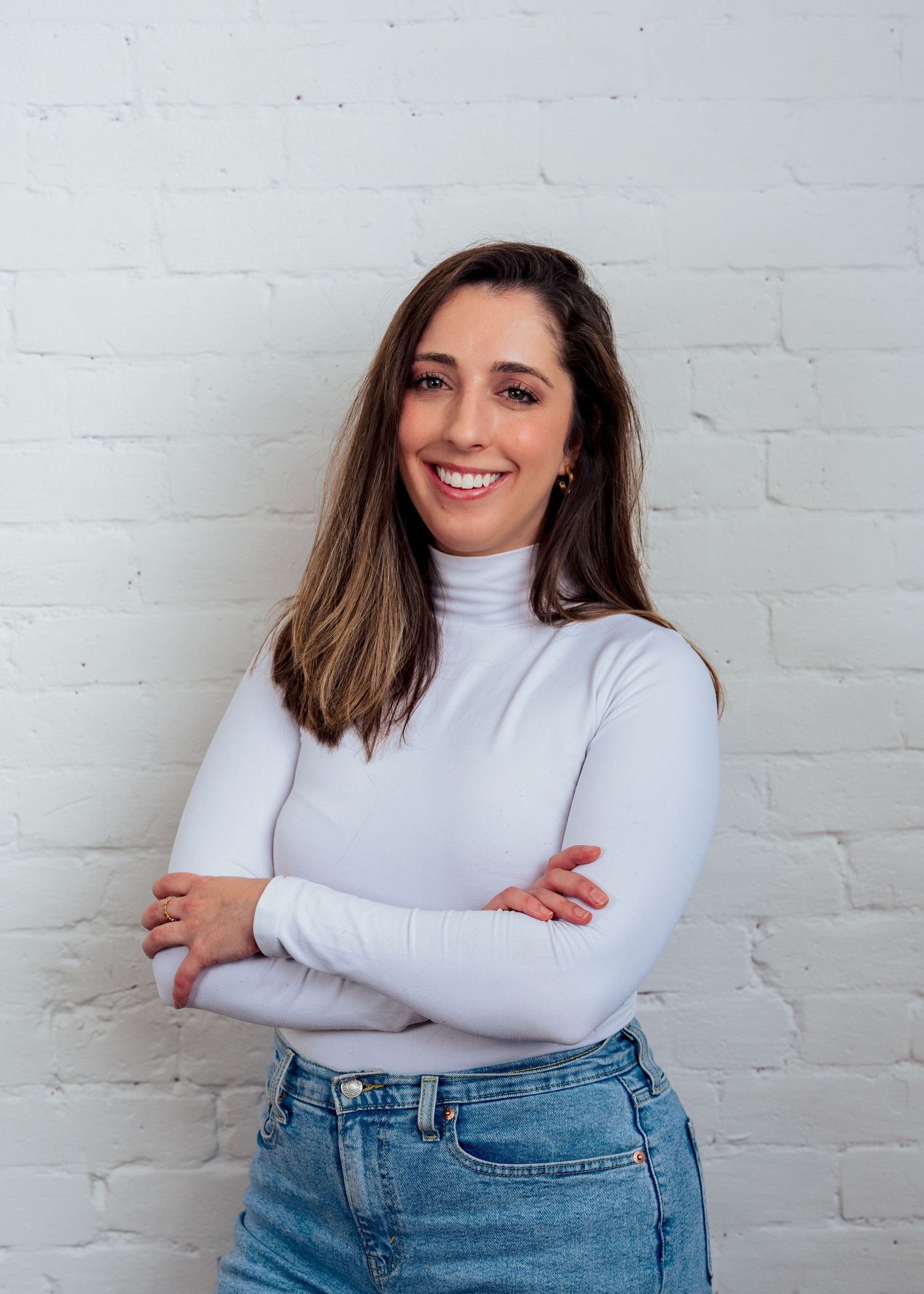 Professional corporate headshot of a smiling woman in a white turtleneck against a brick wall in Northern Colorado