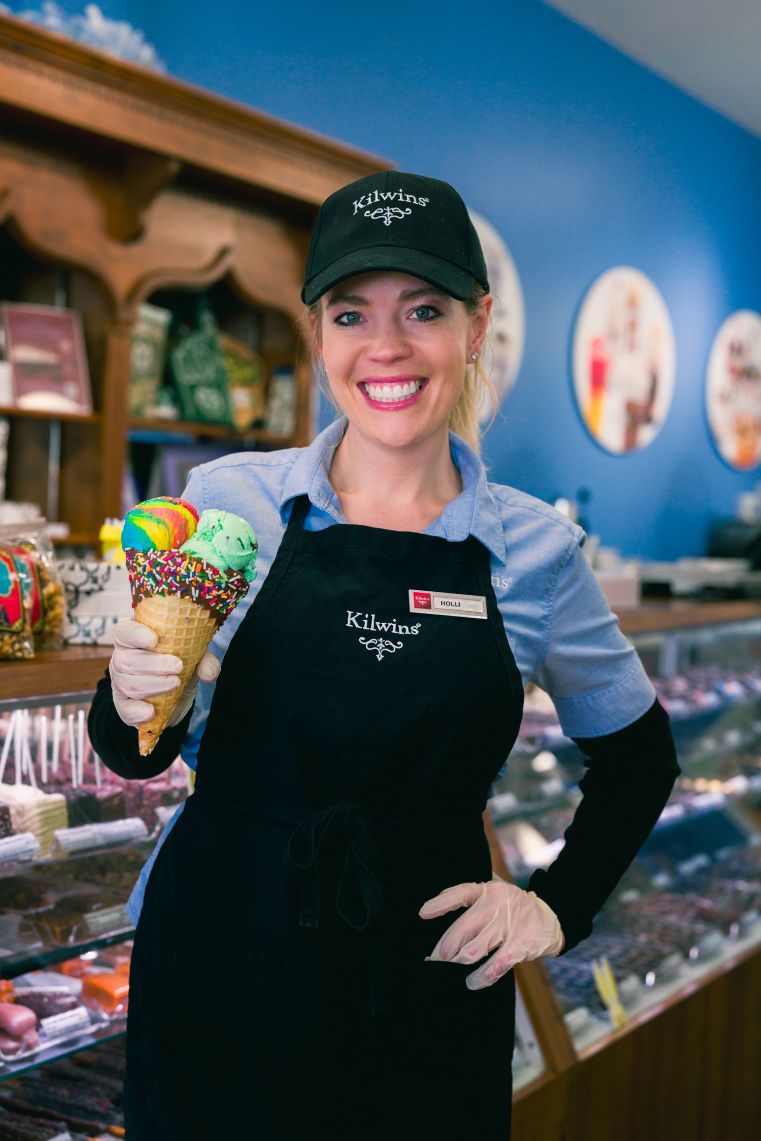 Commercial headshot of a smiling ice cream shop employee holding a decorated cone inside Kilwins in Northern Colorado