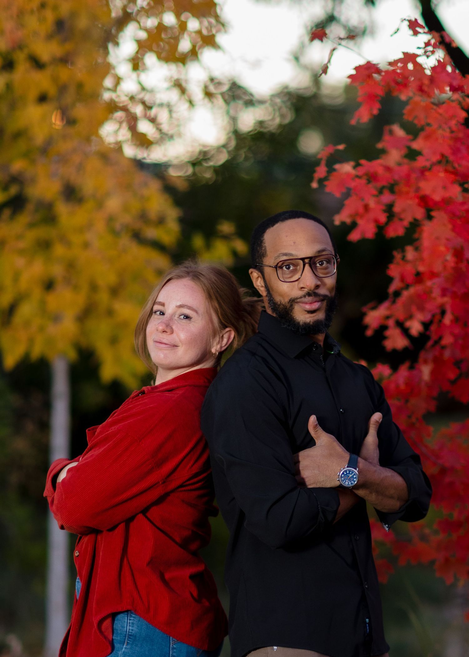 Couple posing back-to-back outdoors surrounded by vibrant red and yellow autumn trees in Northern Colorado