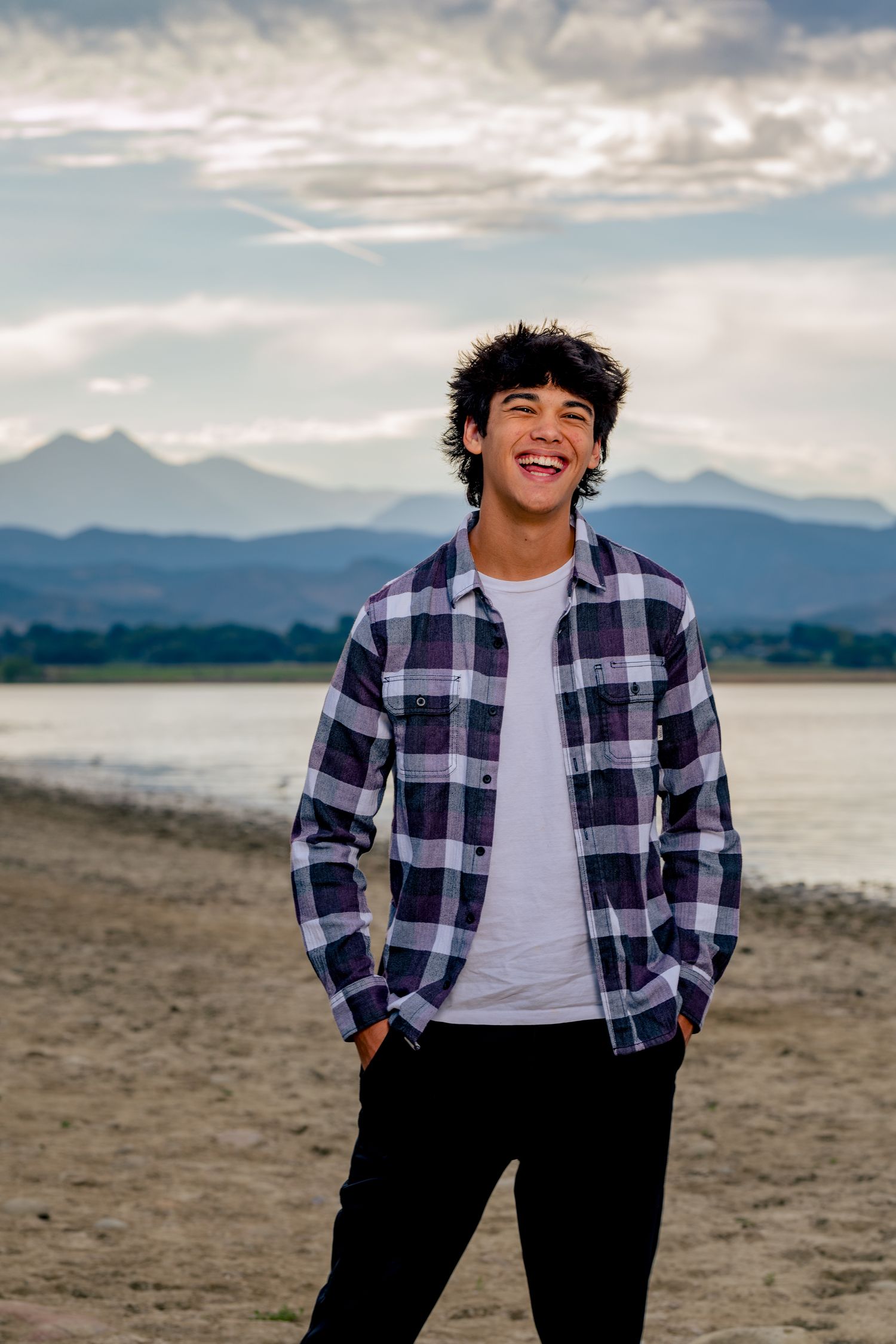 Outdoor senior photo of a teenage boy smiling in front of mountain foothill views in Northern Colorado