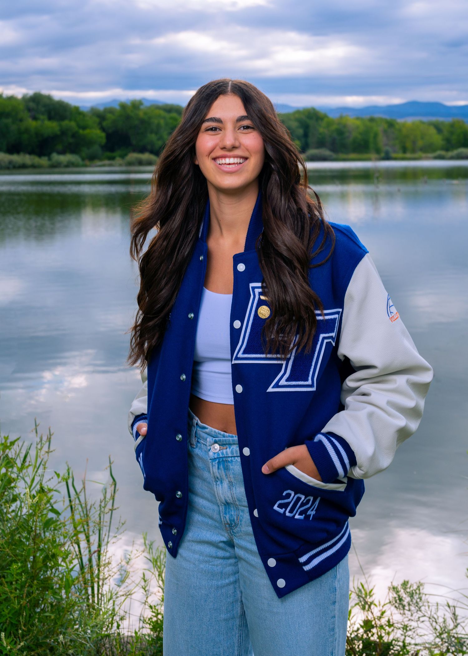 High school senior girl wearing a letterman jacket posing near a lake in Northern Colorado