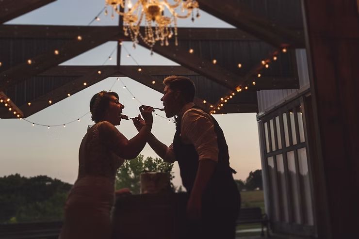 same sex couple eating cake at their iowa barn wedding
