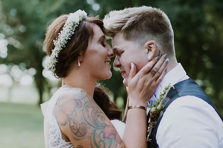 lgbtq bride and groom in embrace with groom crying and bride holding the grooms face