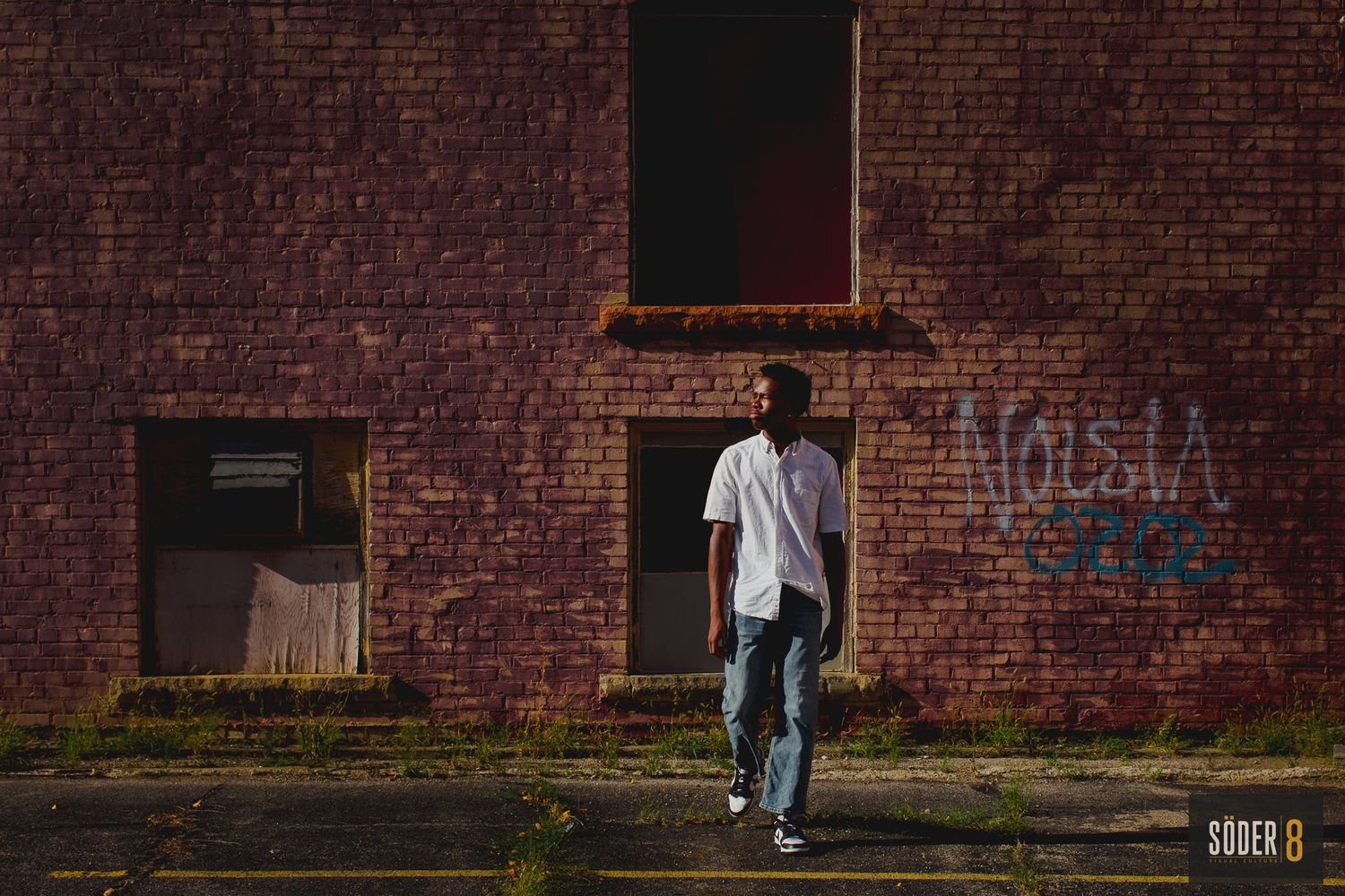 young man walking away from brick wall in light and shadow