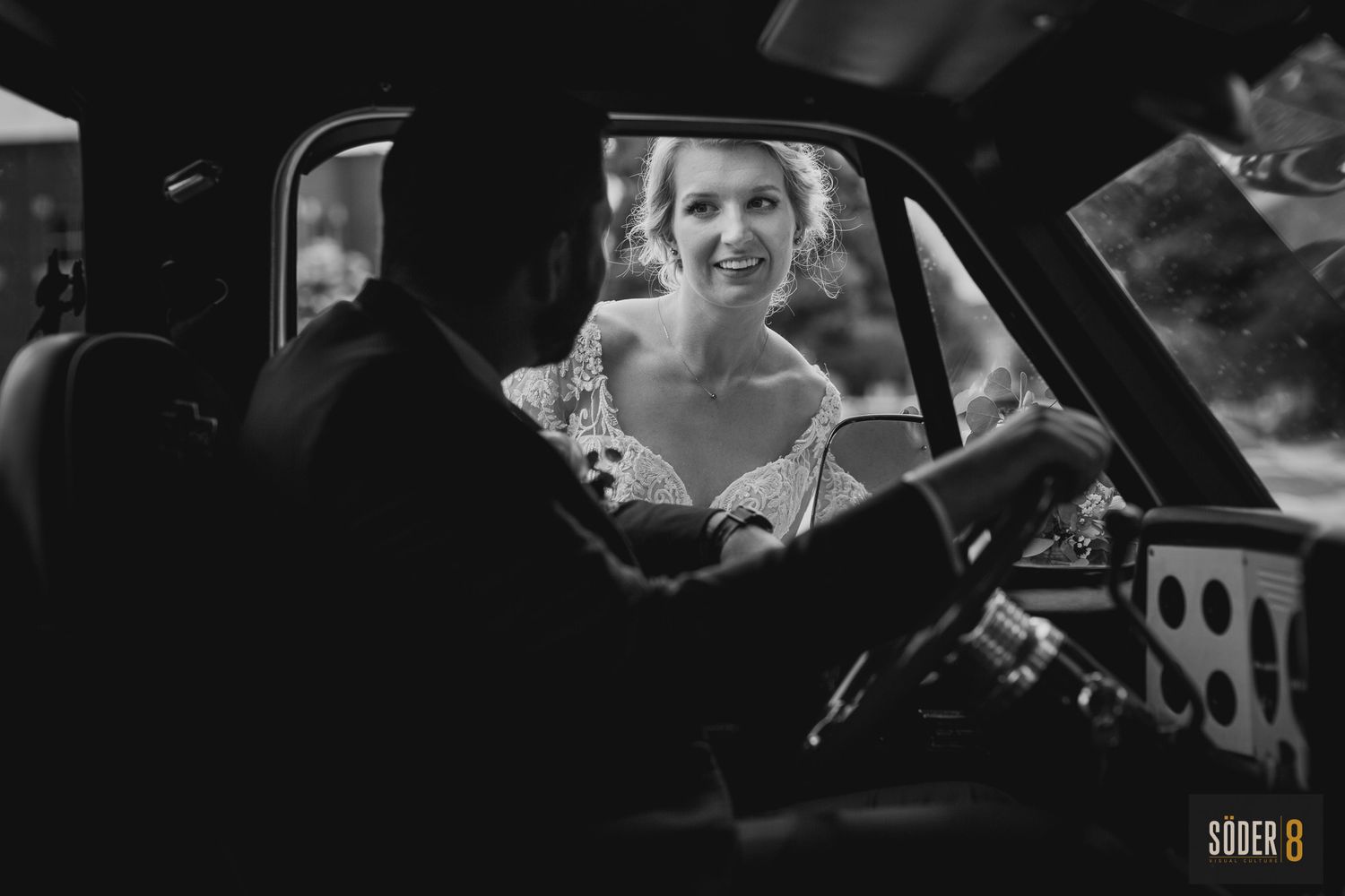 black and white photo of bride peeking in truck window at groom
