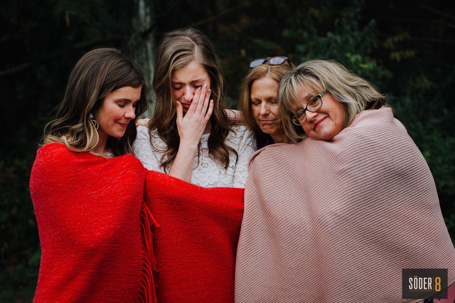 tearful bride huddled with family under blanket