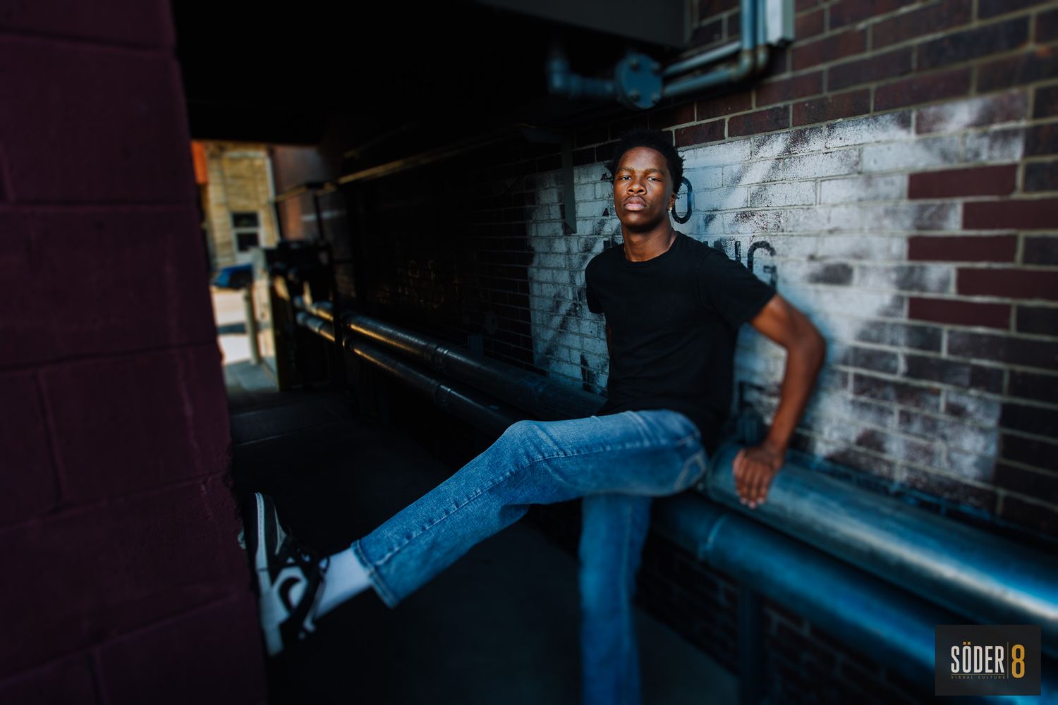 senior photo of young man in alleyway with foot pressed against wall