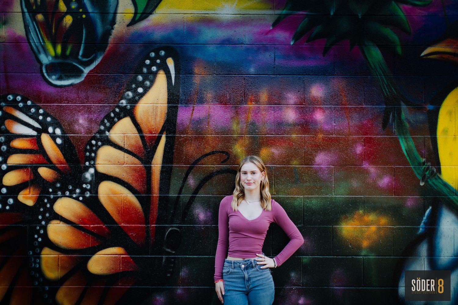 girl in front of large butterfly mural for her senior photos
